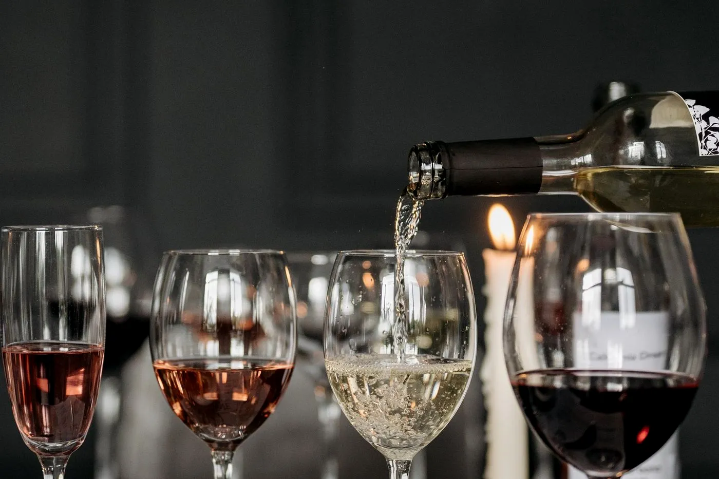 White wine poured into a glass beside a candlelit flight of ros&eacute; and red